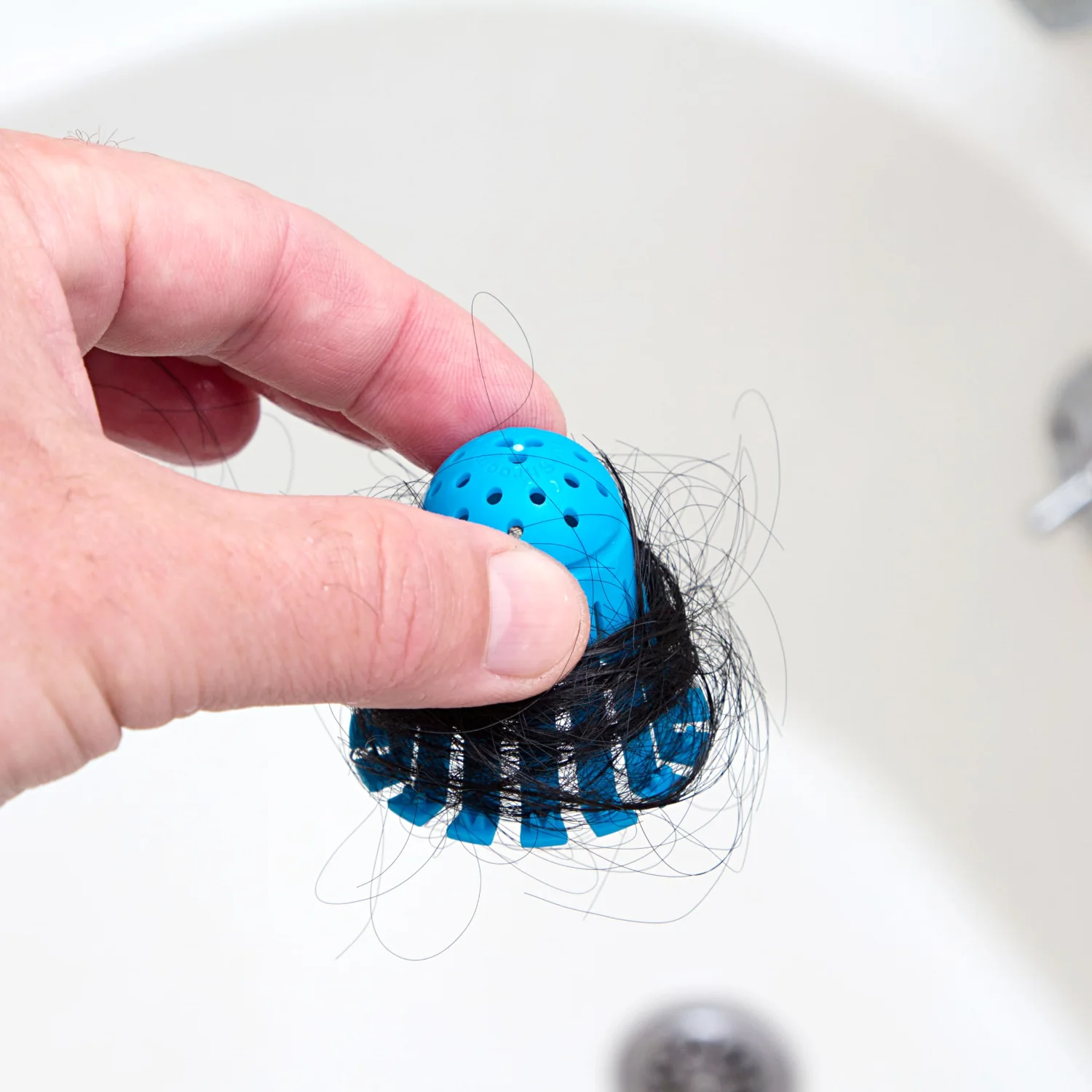 A disposable catcher lifted out of a tub drain: the hair that would otherwise hang from the crossbar.